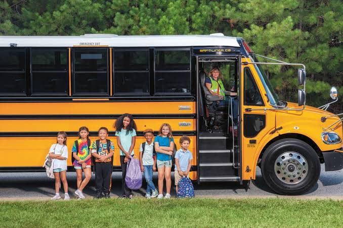 Students standing beside a TravelSafe Transportation school bus with the driver at the door